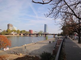 Foto eines Flusses mit Uferpromenade und Brücke im Hintergrund
