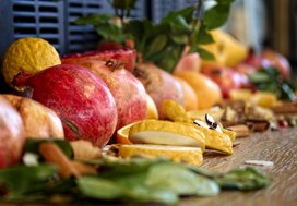 Granatäpfel, Zitronen und grüne Blätter auf einer braunen Holzunterlage