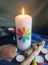 Foto einer erleuchteten weissen Kerze mit Unitarierlogo (stilisierte Blüte mit regenbogenfarbenen Blütenblättern) auf blauer Tischdecke, davor Muscheln, Treibholz und Teelichter