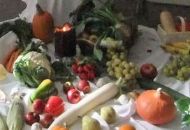 Verschiedenes Obst und Gemüse, unter anderem Äpfel, Trauben, ein Rettich und ein Kürbis auf einer weissen Tischdecke; im Hintergrund ist eine erleuchtete Kerze)